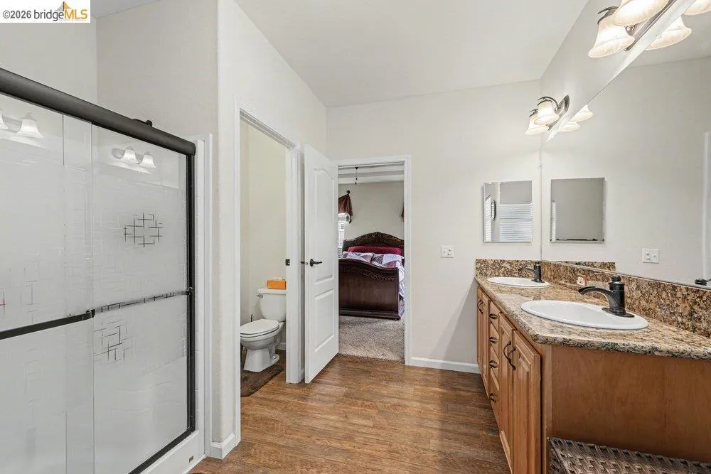 Full bathroom featuring double vanity, dark wood-style flooring, a stall shower, and connected bathroom Full bathroom featuring double vanity, dark wood-style flooring, a stall shower, and connected bathroom