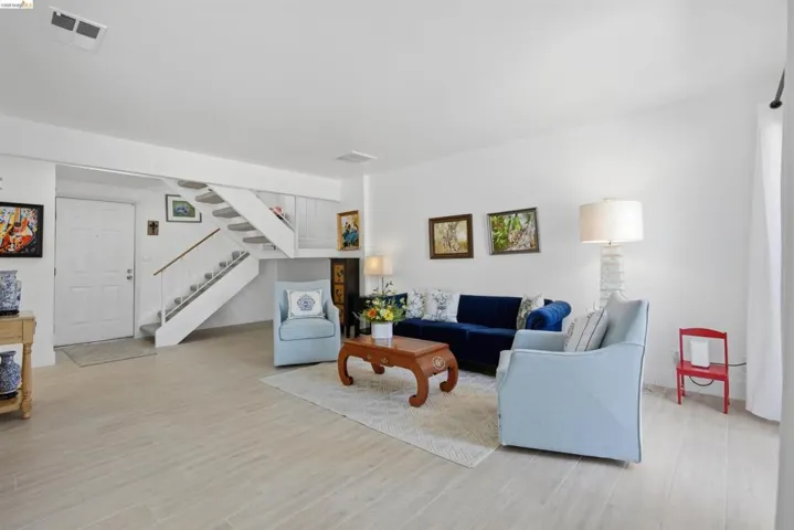 Open-concept living space with light wood-finish flooring, white walls, and a visible staircase