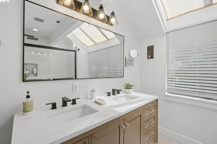 Bathroom featuring a dual vanity with undermount sinks, matte black fixtures, and a skylight