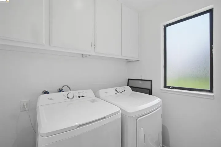 Dedicated laundry area featuring overhead white cabinetry, a single frosted window, and white textured walls