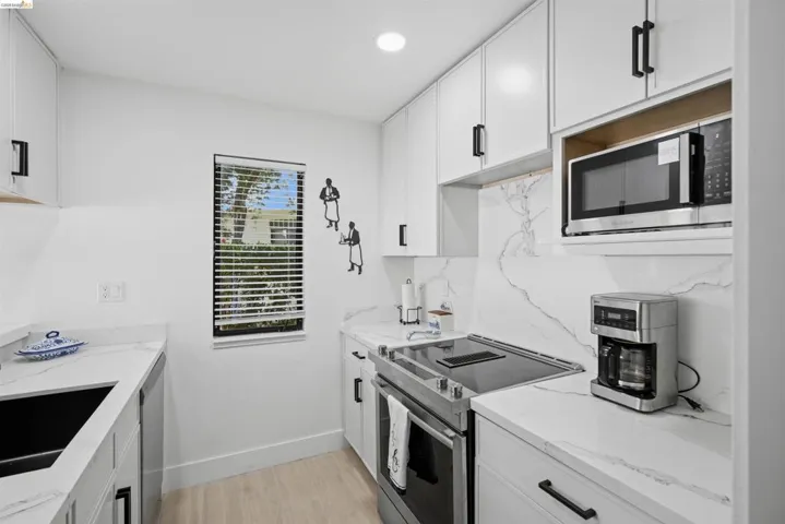 Kitchen featuring white shaker cabinetry, white countertops with veining, a stainless steel electric range, and a built-in microwave