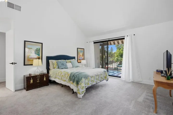Spacious room featuring vaulted ceilings, plush carpeting, a large sliding glass door, and a private balcony