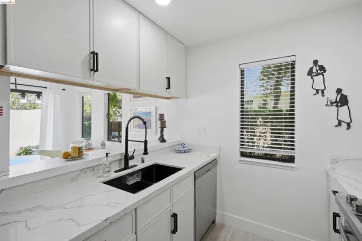 Modern kitchen featuring white shaker cabinetry with black hardware, white stone-finish countertops, a black undermount sink with a black pull-down faucet, and a stainless steel dishwasher