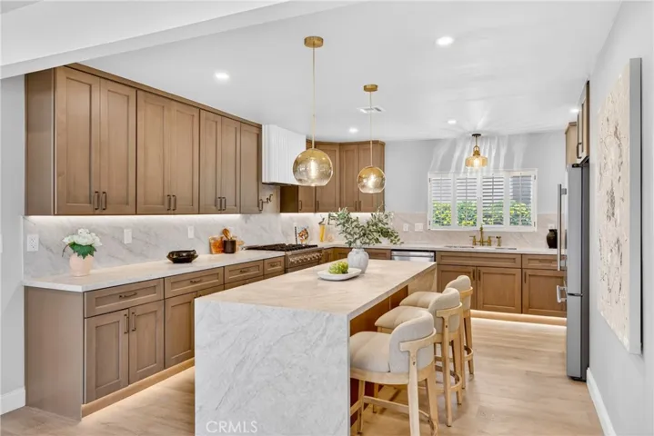 The open-concept kitchen showcases elegant quartzite countertops in a soft Taj Mahal–inspired color palette, adding warmth and sophistication to the space, double-waterfall island, custom cabinetry, and warm designer lighting