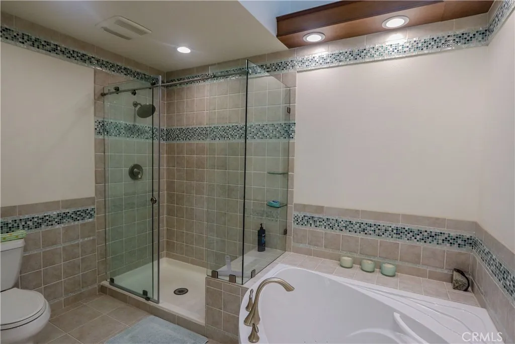 Primary bath with step in tiled shower, spa tub heated floor, and double sinks.