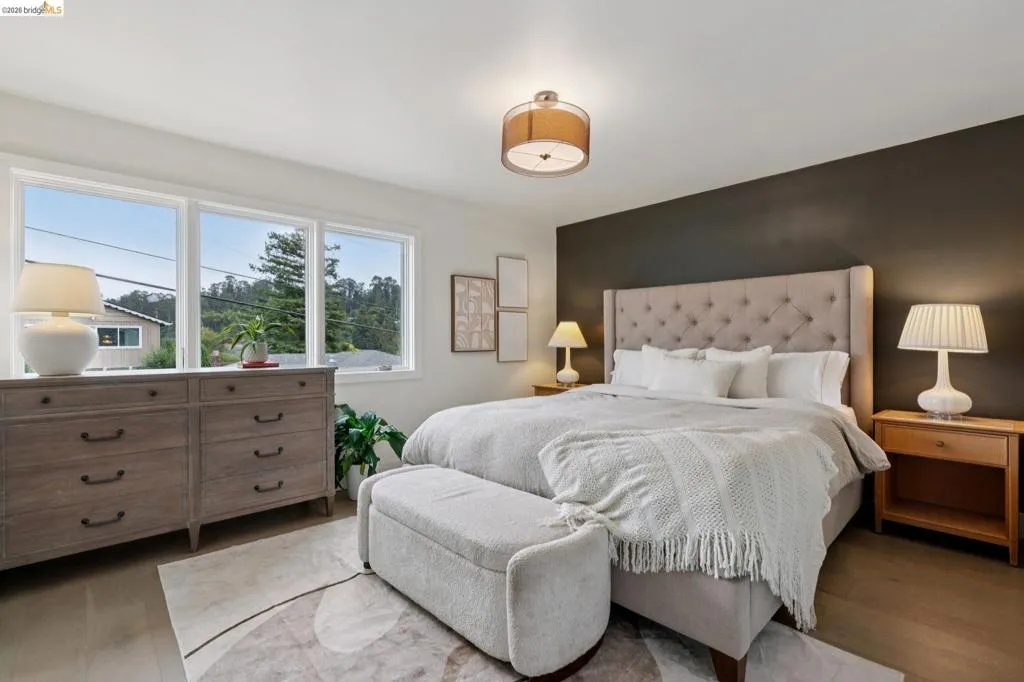 Bedroom featuring a tufted upholstered headboard, a dark accent wall, and wood-finish flooring