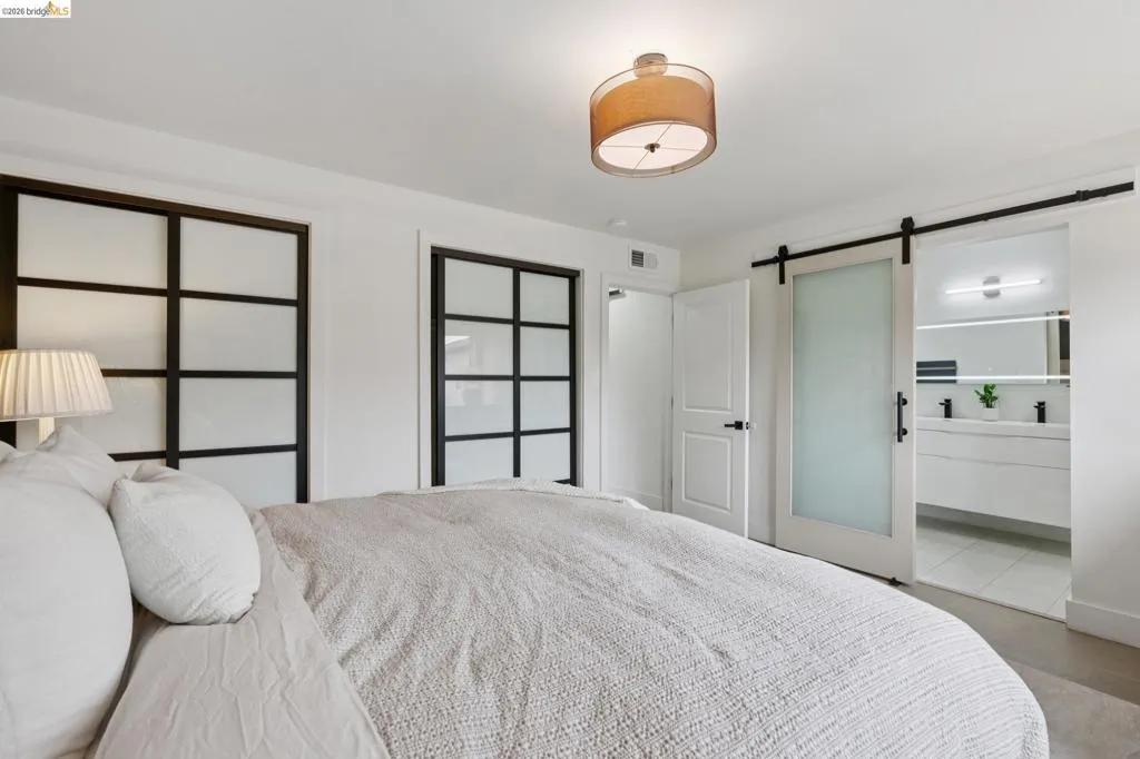 Bedroom featuring a drum pendant light fixture, two multi-pane frosted glass sliding closet doors, and a frosted glass barn door entryway to a bathroom with a double vanity