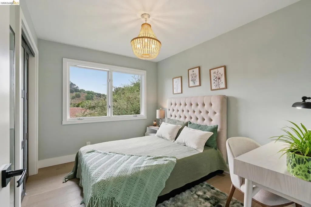 Light-filled room featuring wood-finish flooring, a contemporary chandelier, a window with outdoor scenery, and a paneled door with dark hardware