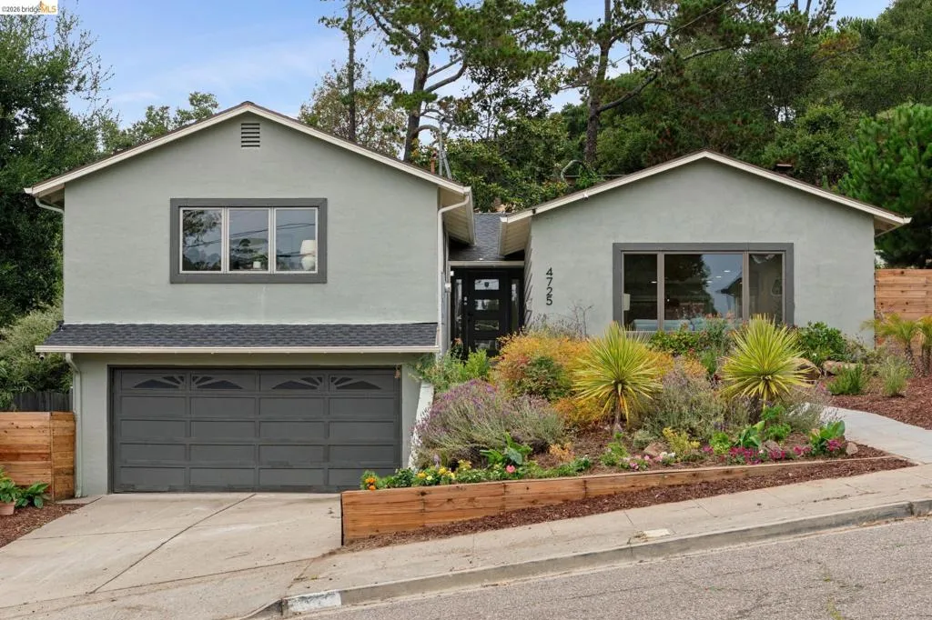 Two-story stucco exterior with a dark gray garage door, multi-pane windows with dark trim, and a gabled roofline