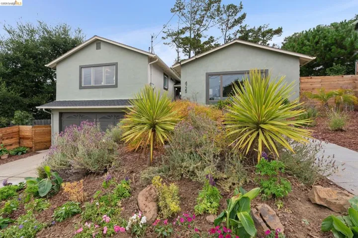 Front elevation with a soft green stucco finish, dark trim windows, and a two-car garage