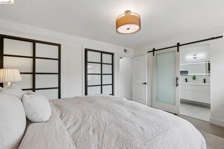 Bedroom featuring a drum pendant light fixture, two multi-pane frosted glass sliding closet doors, and a frosted glass barn door entryway to a bathroom with a double vanity