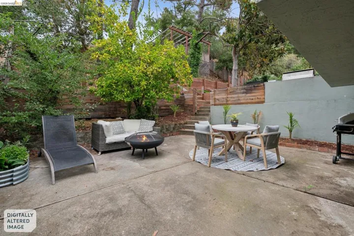 Spacious concrete patio featuring tiered landscaping, a wood retaining wall, and mature trees