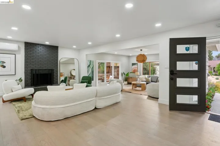 Entry foyer opening into a living space featuring light wood-finish flooring, recessed lighting, and a dark brick fireplace
