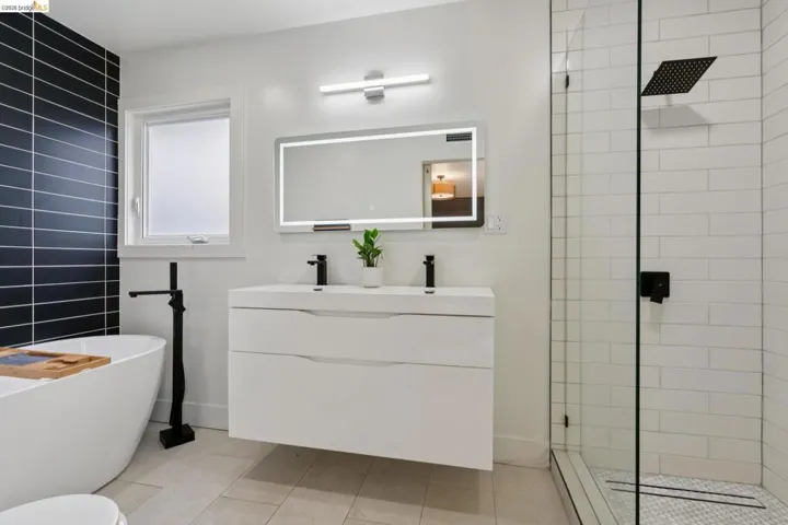 Contemporary bathroom featuring a floating dual-sink vanity with matte black fixtures, an illuminated mirror, and a glass-enclosed shower with white subway tile