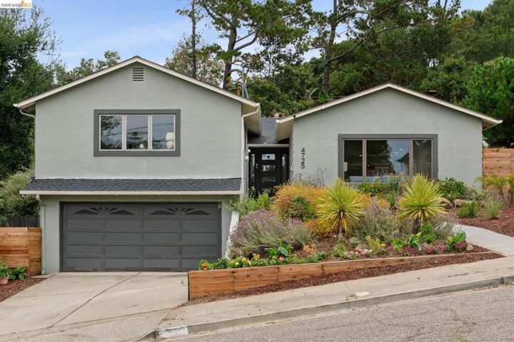 Two-story stucco exterior with a dark gray garage door, multi-pane windows with dark trim, and a gabled roofline