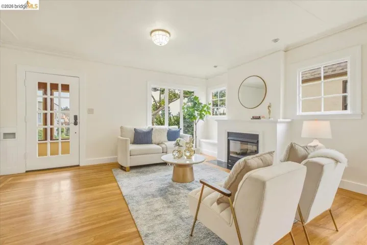 Living area featuring wood-finish flooring, a white trim fireplace with a dark hearth, multiple windows, and a glass-paneled entry door