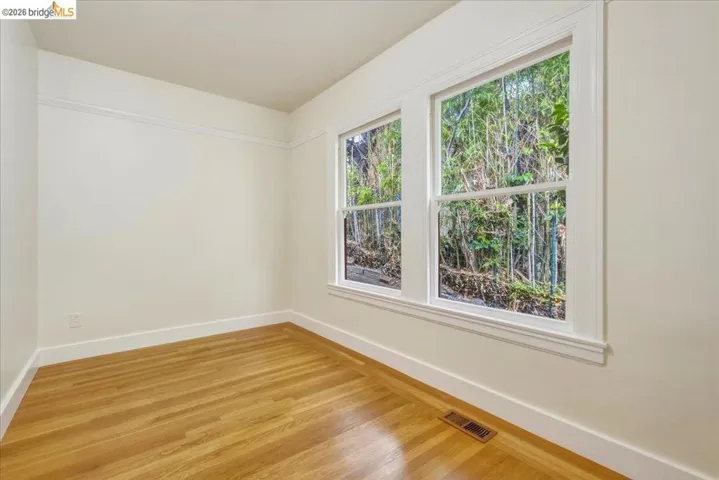 Room featuring two large windows with white trim, wood-finish flooring, a baseboard heating vent, and crown molding