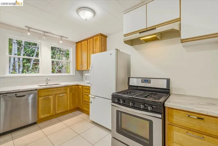 Kitchen featuring light wood cabinetry, stone-finish countertops, stainless steel gas range, stainless steel dishwasher, and tile flooring