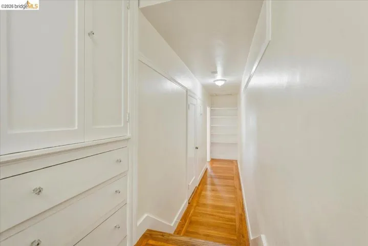 Hallway featuring wood-finish flooring, built-in cabinetry with crystal knobs, integrated shelving, white trim, and a flush-mount ceiling light fixture