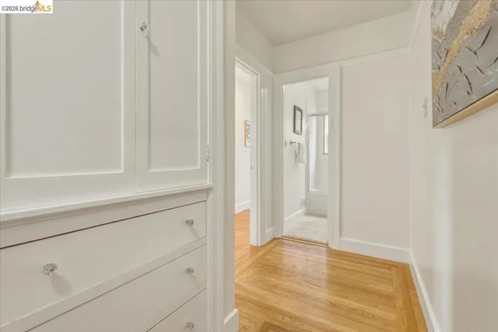 Hallway featuring built-in white cabinetry with crystal knobs, wood-finish flooring, and white baseboards