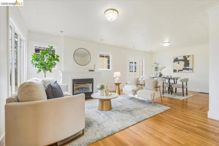 Open-concept living area featuring wood-finish flooring, a contemporary fireplace with a white mantel, and multiple windows providing natural light