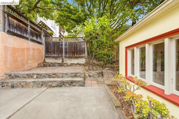 Rear exterior featuring a stucco facade with white-framed windows, a red trim accent, and a concrete patio