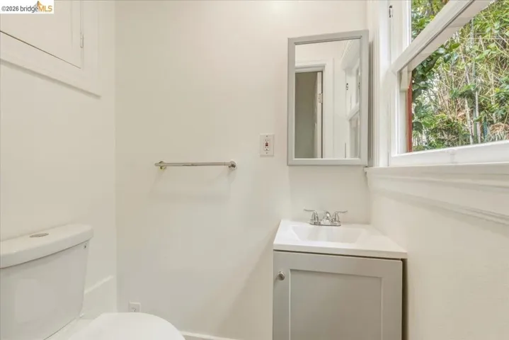 Compact bathroom featuring a white toilet, corner vanity with integrated sink, framed mirror, and a window providing natural light
