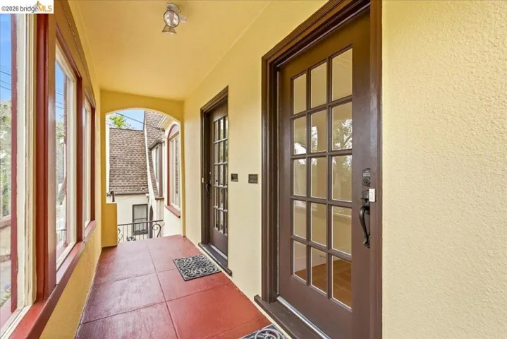 Covered entry porch featuring a paneled door with glass inserts, red tile flooring, textured exterior walls, and multiple casement windows with dark trim