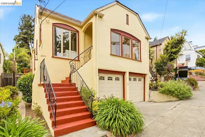 Stucco exterior residence featuring an arched entry, red-trimmed windows, a two-car garage, and a prominent exterior staircase with wrought iron railings