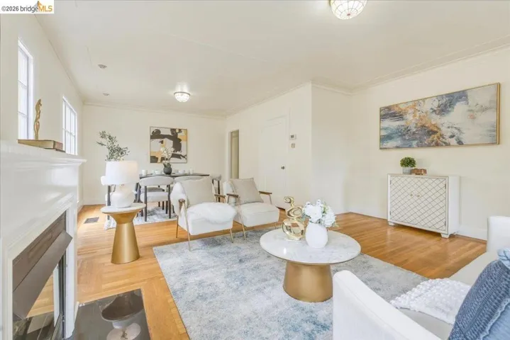 Hardwood flooring throughout, crown molding, and a fireplace with a white mantel and black hearth