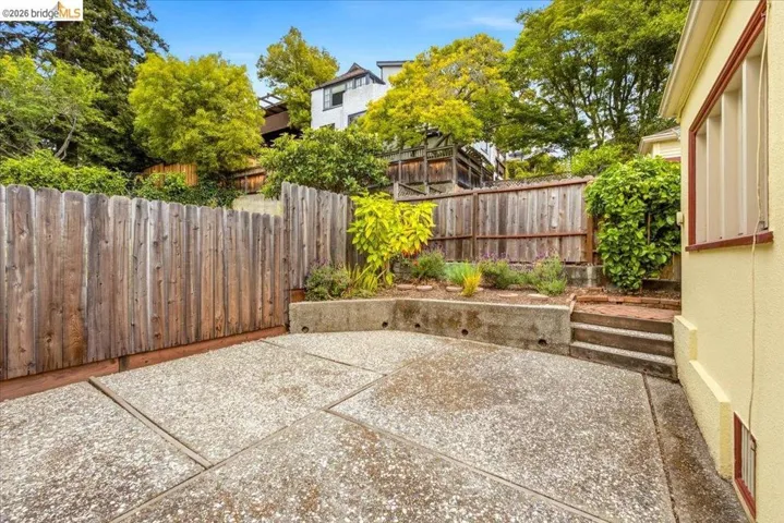 Exposed aggregate patio area featuring geometric scoring, wood fencing, and a terraced planter with established greenery