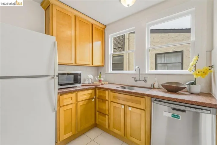 Kitchen featuring light wood cabinetry, white appliances, and a stainless steel dishwasher