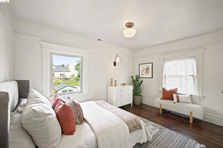 Bright bedroom featuring rich wood-finish flooring, white trim, and two windows