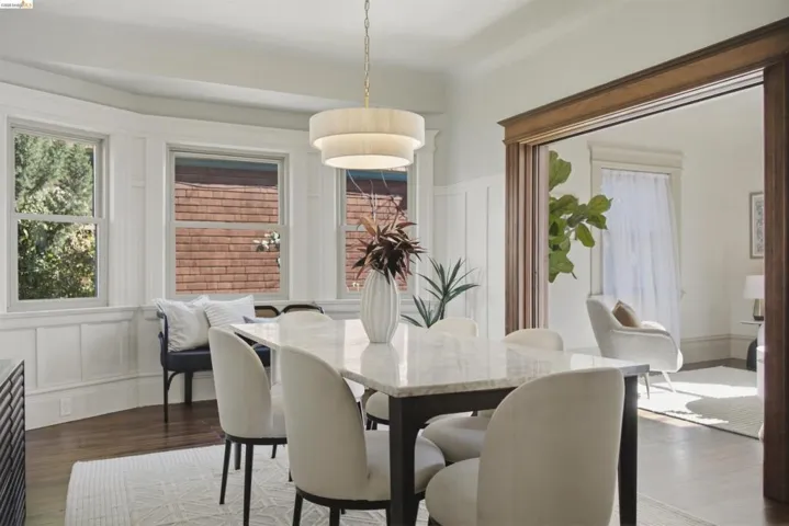 Dining area featuring a tiered drum pendant light fixture and a bay window with white wainscoting