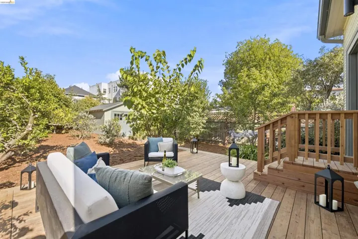 Expansive wood-finish decking featuring a built-in staircase with wood railing, surrounded by mature trees and landscaping