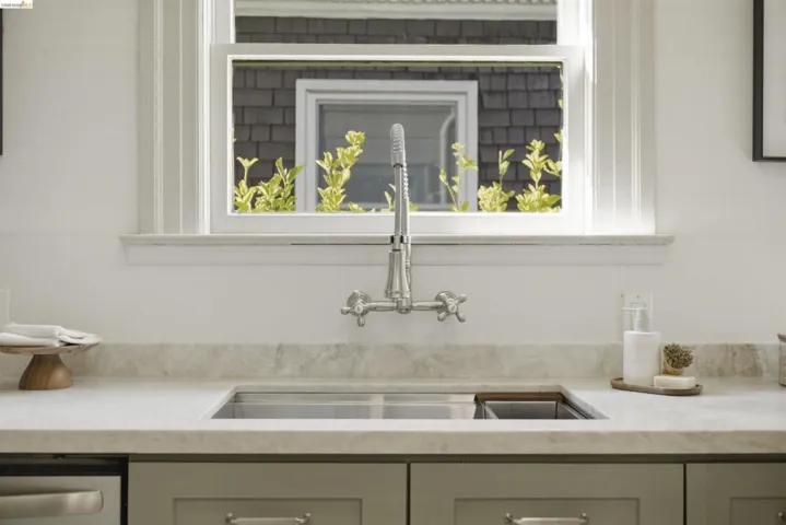 Kitchen sink area featuring a wall-mounted faucet with dual handles, a stainless steel undermount sink, and a light-toned countertop