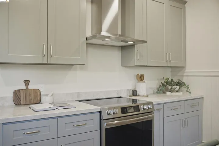 Contemporary kitchen featuring two-tone cabinetry, stainless steel range with overhead hood, and light-toned countertops