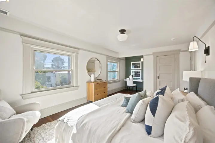 Spacious room featuring wood-finish flooring, two windows with traditional trim, a built-in desk area with shelving, and a paneled door