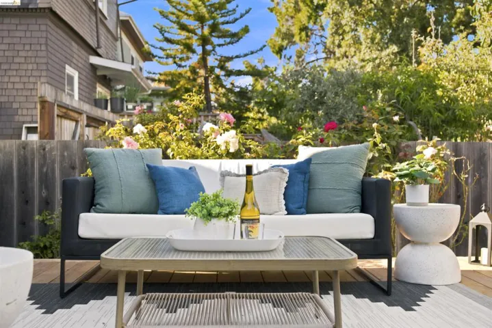 Outdoor wood-finish deck with a woven area rug, surrounded by a wood fence and mature landscaping
