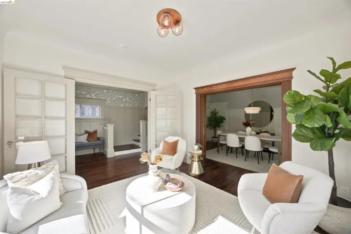 Bright living area featuring dark wood-finish flooring, a contemporary ceiling light fixture, and an arched entry to a dining space with a modern chandelier