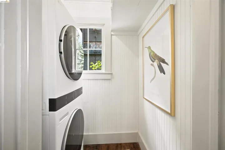 Dedicated laundry area featuring a stacked washer and dryer, beadboard paneling, a double-hung window, and wood-finish flooring