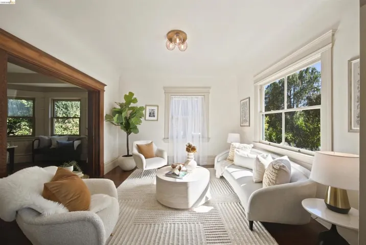 Bright living area featuring wood-finish flooring, ample natural light from large windows, a decorative ceiling fixture, and classic white trim throughout