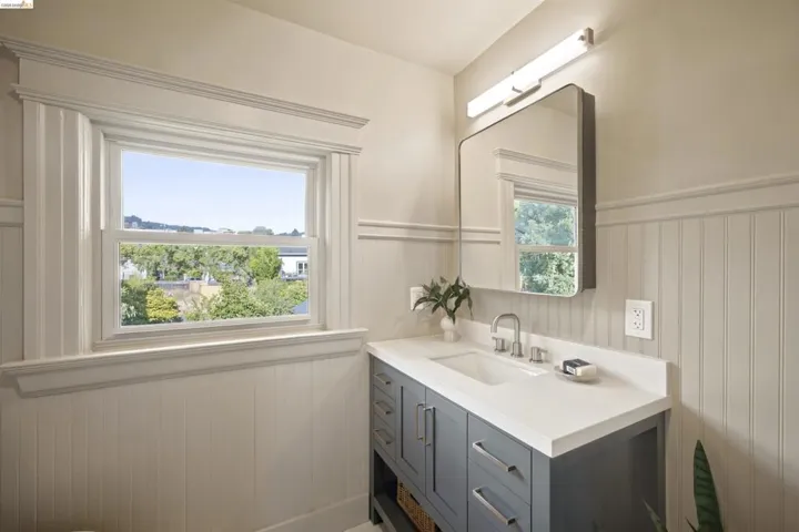 Bathroom featuring a single window, beadboard wall paneling, a rectangular mirror, a light bar fixture, and a vanity with a white countertop and undermount sink