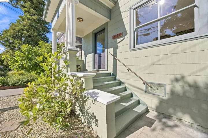 Light green horizontal siding exterior with a multi-pane window, entry porch featuring decorative columns, and a front staircase with a handrail