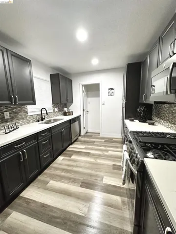 Modern kitchen featuring dark cabinetry, light countertops, wood-finish flooring, a mosaic tile backsplash, and stainless steel appliances