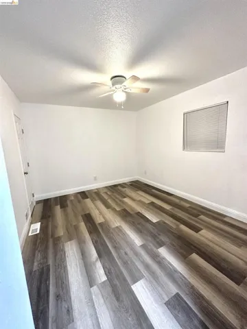 Spacious room featuring multi-tone wood-finish flooring, white baseboards, and a ceiling fan with light fixture