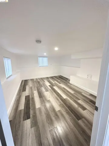 Spacious room featuring wood-finish flooring, recessed lighting, and bright white walls