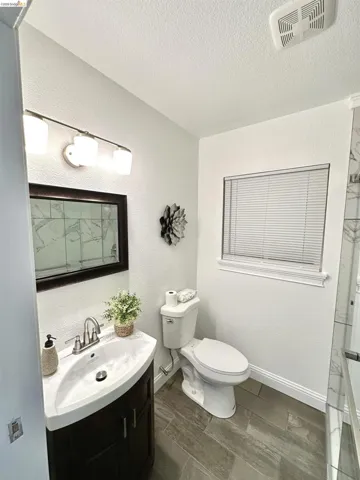Bathroom featuring a dark wood-finish vanity with an integrated white sink, a modern three-light fixture, wood-look tile flooring, and a window with blinds