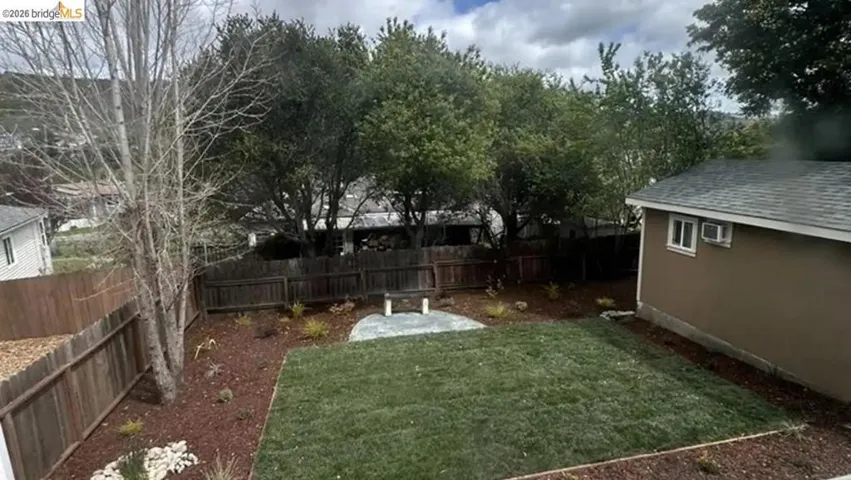 Expansive backyard featuring a manicured lawn, fresh mulch landscaping, mature trees, and a wooden privacy fence