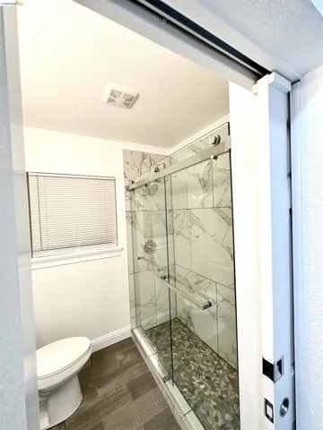 Glass-enclosed shower with a pebble-stone floor and white marble-look tile surround